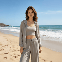 A young woman is wearing gray sun-protective wide-leg pants, with a beach in the background
