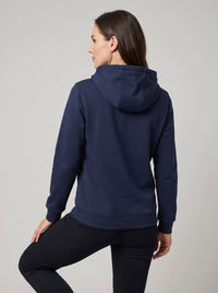 A woman wearing a navy blue pullover heated hoodie, shown from the back, paired with black leggings.