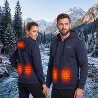 A man and a woman wearing navy blue heated hoodies stand in a snowy mountain landscape by a river. The hoodies have glowing orange heat-map graphics showing heated zones on the back and front torso.