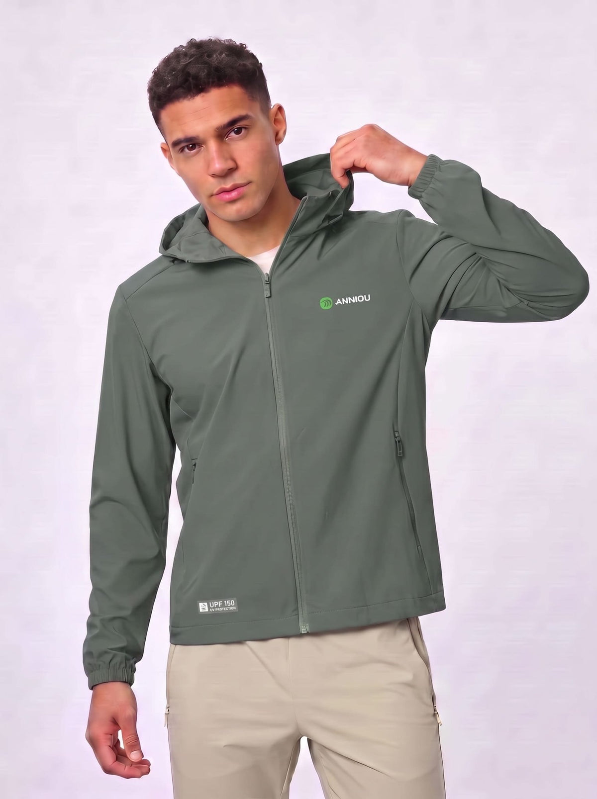 A man wearing a sage green hooded jacket with a full zipper and a small green and white Anniou logo on the left chest, paired with beige pants, against a light gray studio background.