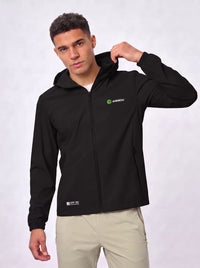 A man wearing a black zip-up hooded jacket with a green and white 'Anniou' logo on the left chest, paired with beige pants, against a light gray studio background.