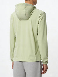 A person shown from the back wearing a light sage green hooded jacket and gray sweatpants against a plain white studio background.