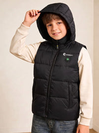 A boy wearing a black heated hooded puffer vest over a cream long-sleeve shirt and blue jeans.