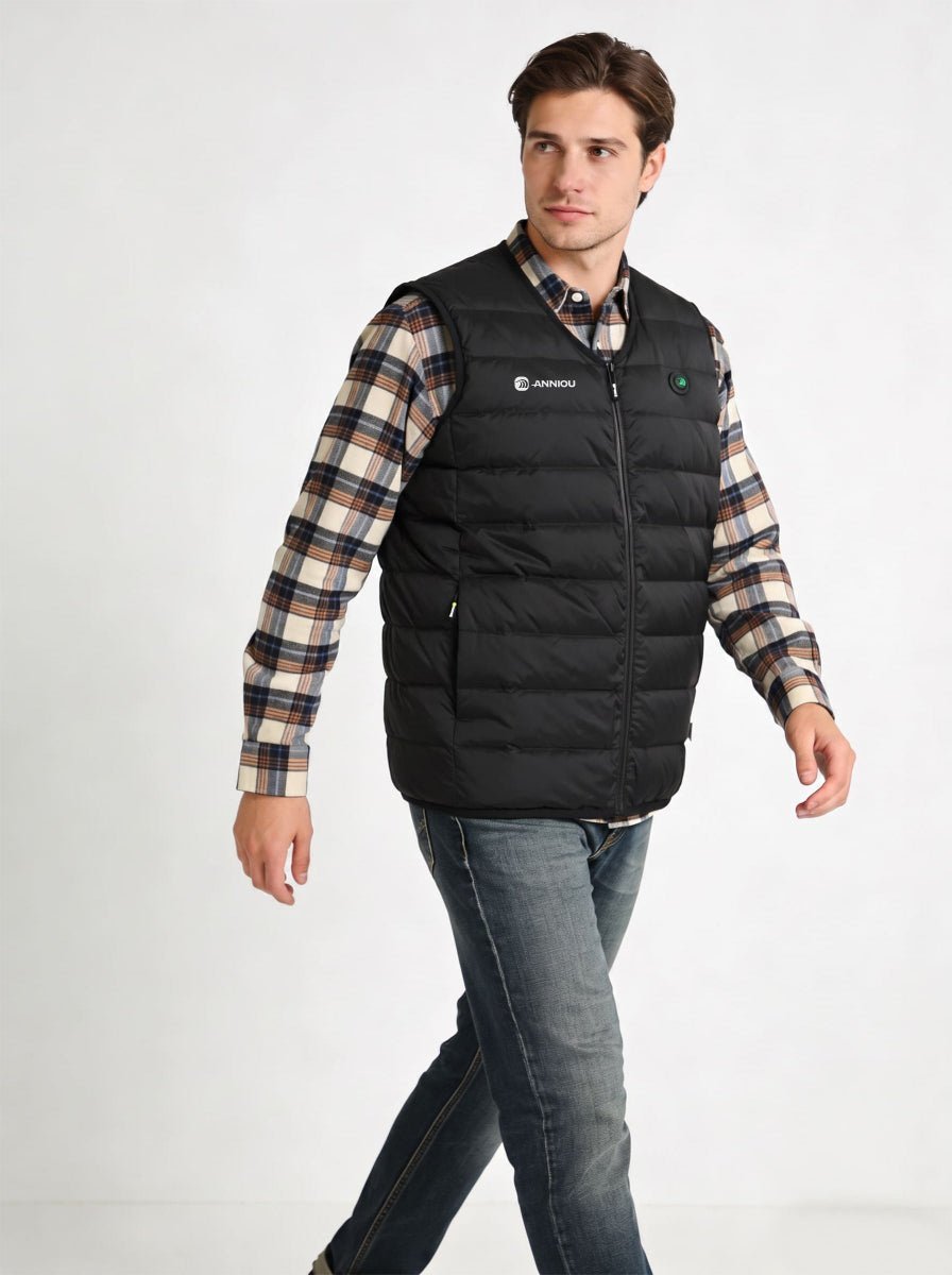 A man wearing a black heated puffer vest over a beige and brown plaid flannel shirt, paired with blue jeans, photographed against a plain white studio background.
