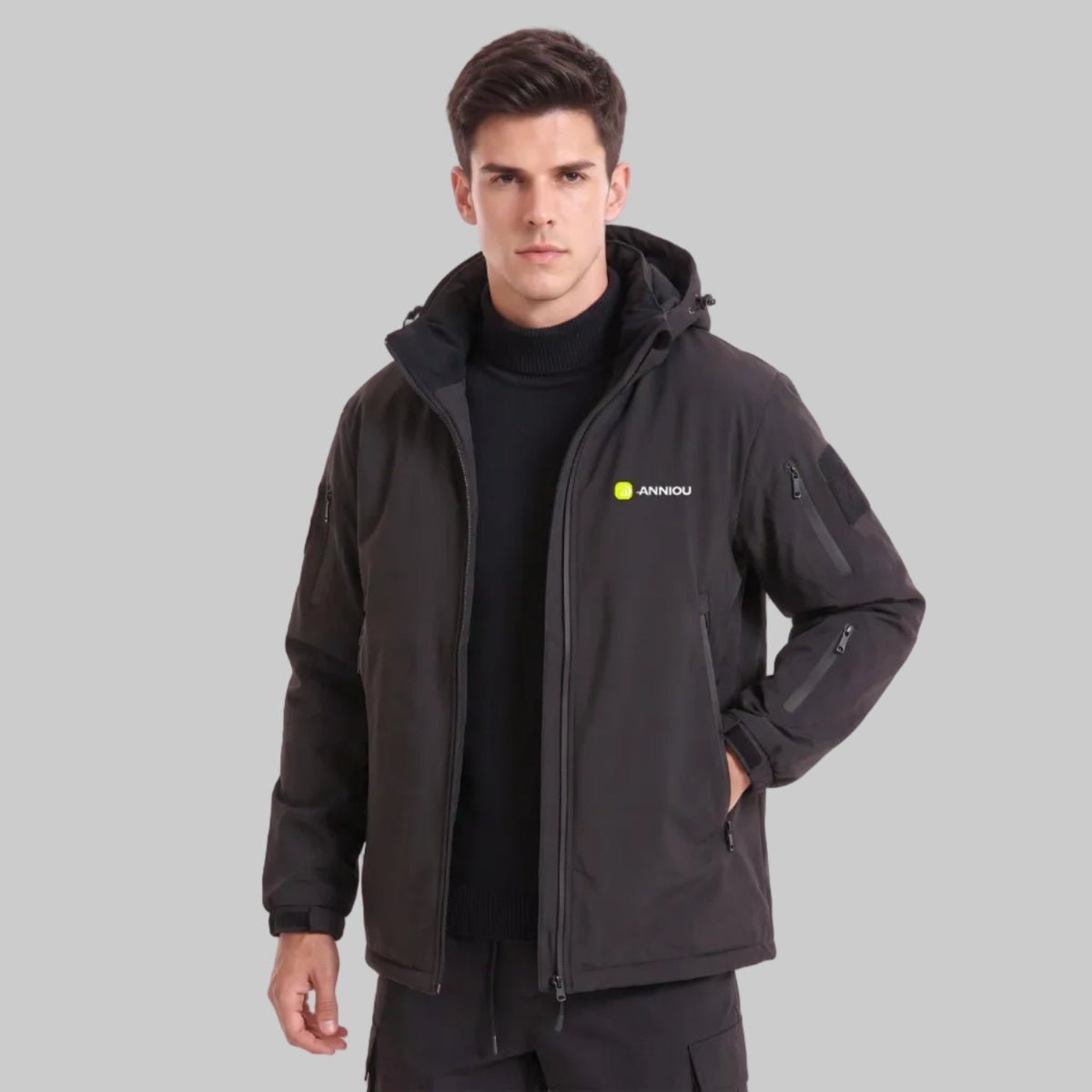 Young British male model in ANNIOU black tactical hooded jacket, half unzipped, one hand inside pocket
