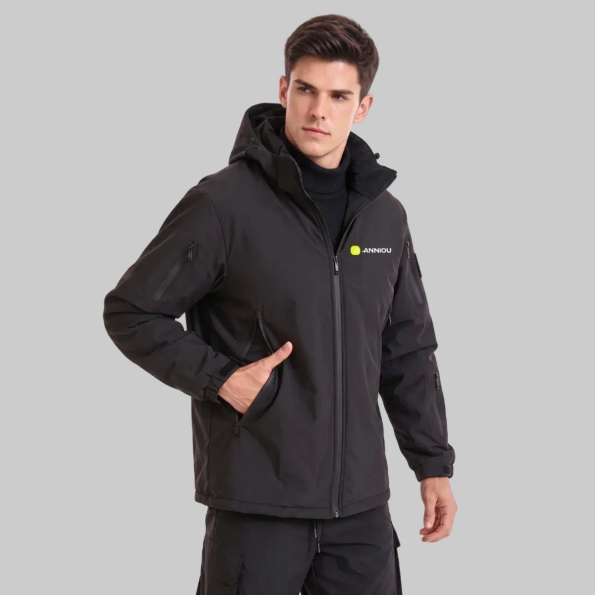 Young British male model wearing ANNIOU black hooded tactical softshell jacket, one hand in side pocket,