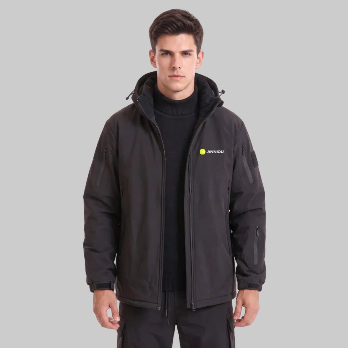 Front view of young British male model, ANNIOU black hooded tactical jacket fully unzipped, black turtleneck inside