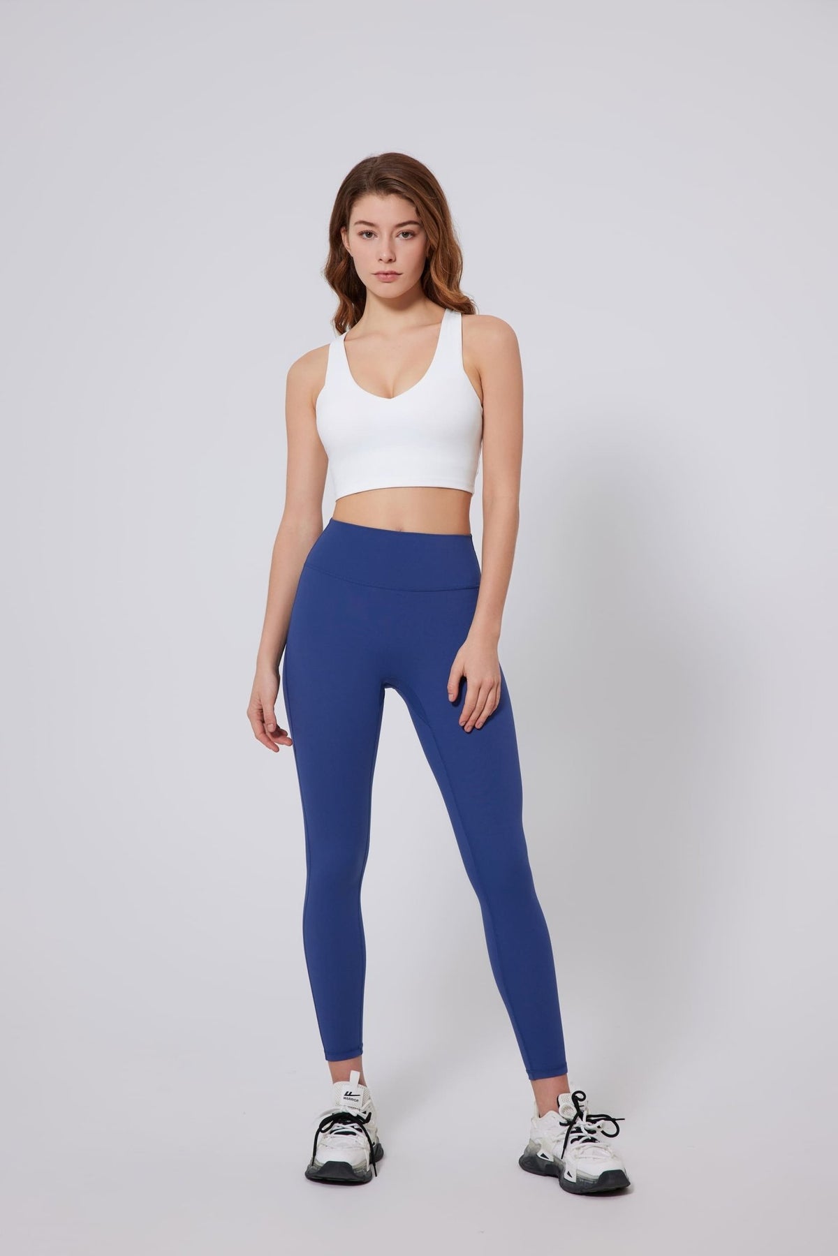 Woman wearing a UPF 50+ white sports bra and blue leggings on a gray background