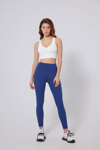 Woman wearing a UPF 50+ white sports bra and blue leggings on a gray background