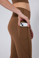 Person wearing brown leggings with a pocket holding a phone on a plain background