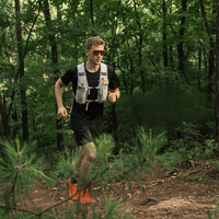 A man is carrying a sports water bottle, with a forest in the background.