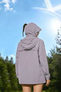 Person wearing a light gray hooded jacket in a forest with a clear blue sky.