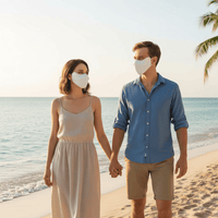 Man and woman holding hands on a beach wearing face masks.