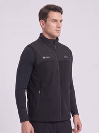 A man wearing a black zip-up fleece heated vest over a black long-sleeve shirt.