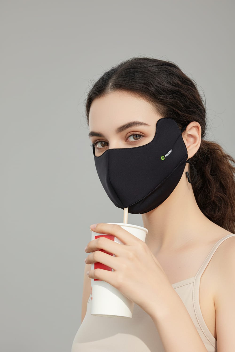Woman wearing a black face mask and holding a cup against a gray background