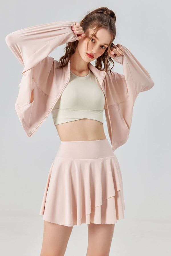 Woman wearing a light pink jacket, green crop top, and pink skirt on a white background