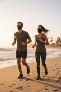 Two people running on a beach at sunset with face masks on