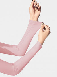 A close-up of a person's forearms and hands stretching a light pink, long-sleeve compression sleeve or arm warmers against a plain light gray background.