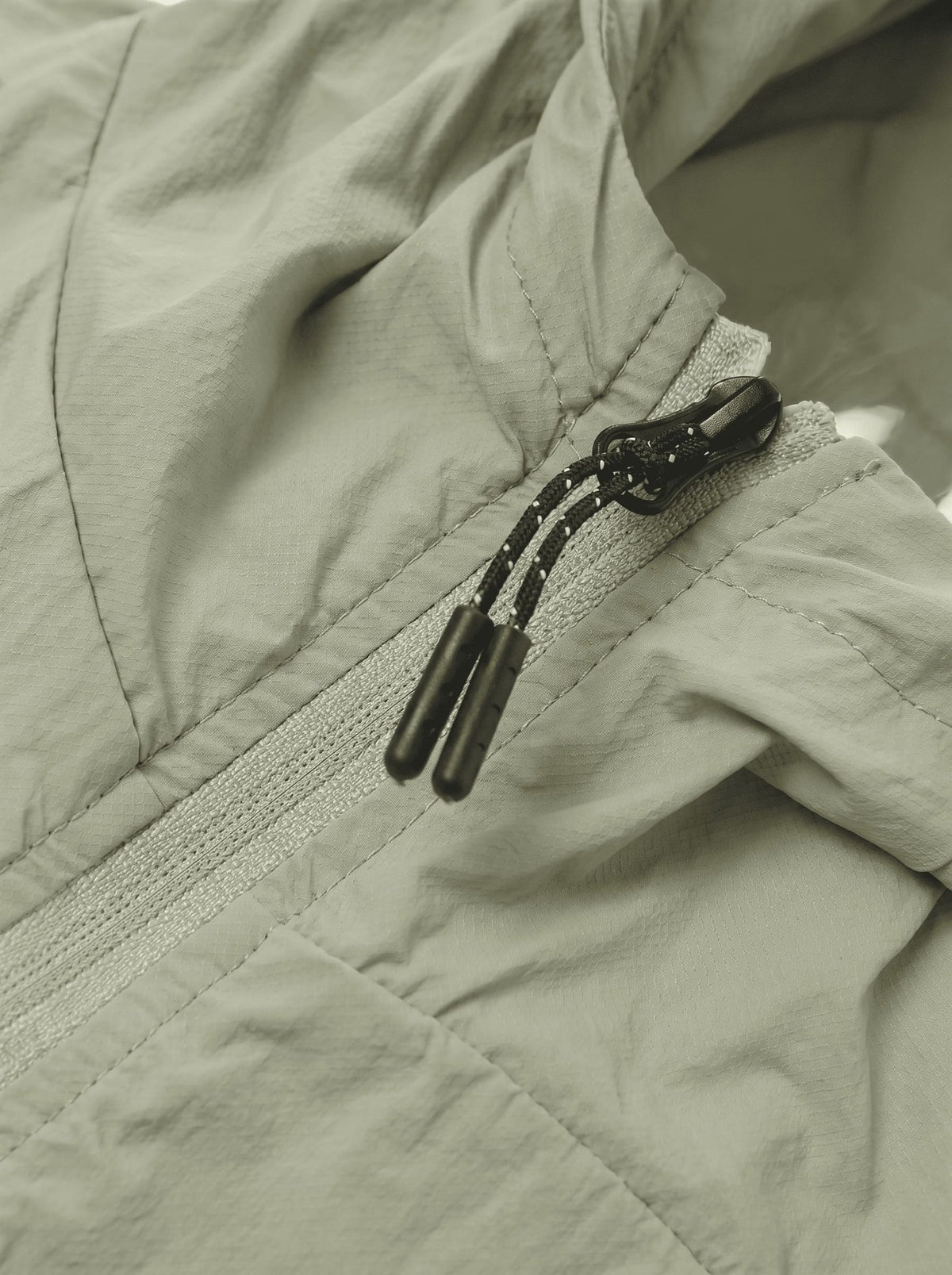 Close-up of a light sage green lightweight jacket with a black drawstring zipper.