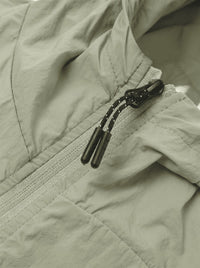 Close-up of a light sage green lightweight jacket with a black drawstring zipper.