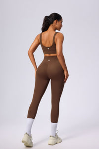 Woman wearing a brown sports bra and leggings set on a light gray background