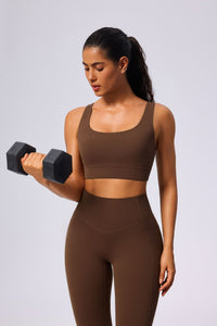 Woman in brown athletic wear lifting a dumbbell against a light gray background