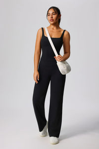 Woman wearing a black jumpsuit holding a white bag on a light gray background