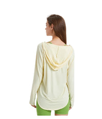 Woman wearing a upf 100+ light yellow long-sleeve top with hood and green pants on a white background