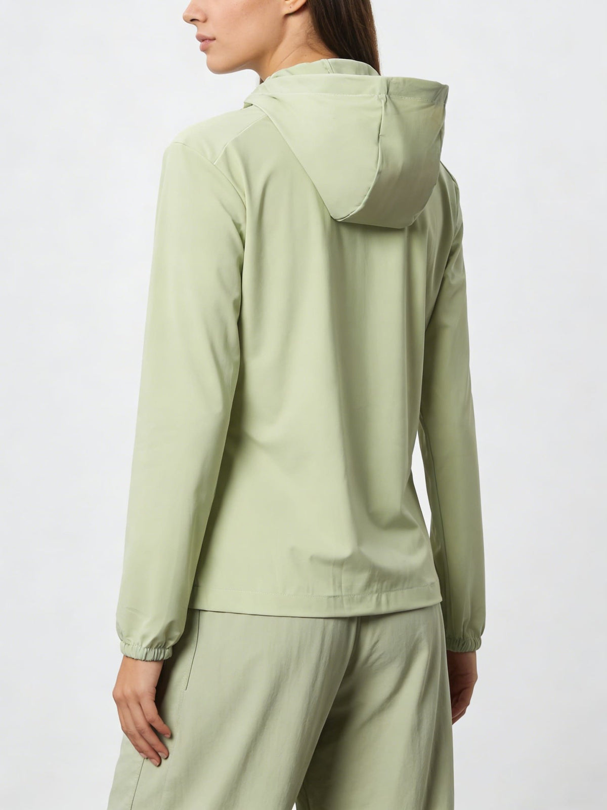 Person wearing a lightgreen jacket with a hood and pants on a white background