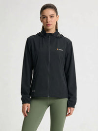 A woman modeling a black hooded zip-up jacket with a small orange and white Anniou logo on the left chest, paired with olive green leggings, against a light gray studio background.