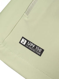Close-up of a light sage green fabric item showing a black rectangular label that reads 'UPF 150 UV PROTECTION' near a zipper.