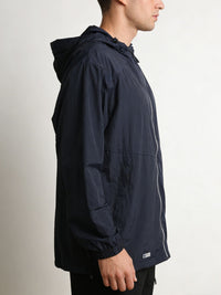 A man shown in profile wearing a dark navy hooded jacket with a front zipper and a small white logo patch near the hem, photographed against a plain light background.