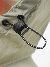 Close-up of a beige lightweight fabric garment with a black drawcord and black plastic toggle closure.