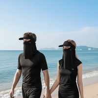 Two people wearing black sun visors and face coverings on a beach.