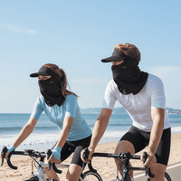 Two people riding bicycles on a beach wearing face masks.