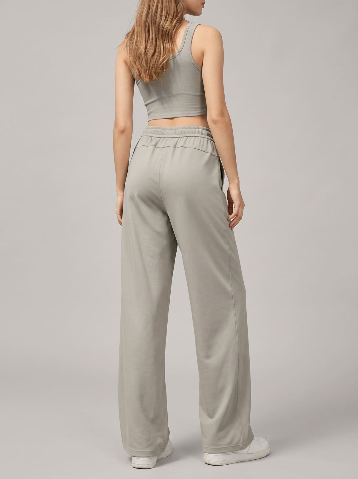 A woman shown from the back wearing a light gray ribbed crop top and matching wide-leg sweatpants, standing against a neutral light gray studio background.