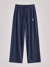 A pair of navy blue wide-leg athletic pants with an elastic waistband and drawstring, featuring a small white embroidered logo on the left thigh, shown against a light gray background.