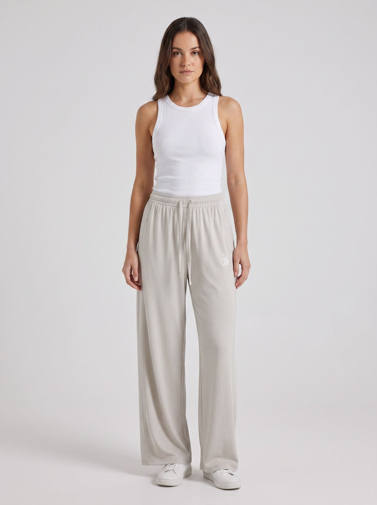 A woman modeling a white ribbed tank top and light gray wide-leg drawstring pants against a plain light gray studio background.