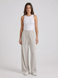 A woman modeling a white ribbed tank top and light gray wide-leg drawstring pants against a plain light gray studio background.