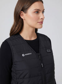 A woman wearing a black quilted puffer vest with a white 'ANNIOU' logo on the left chest, layered over a black long-sleeve top, photographed against a light gray studio background.