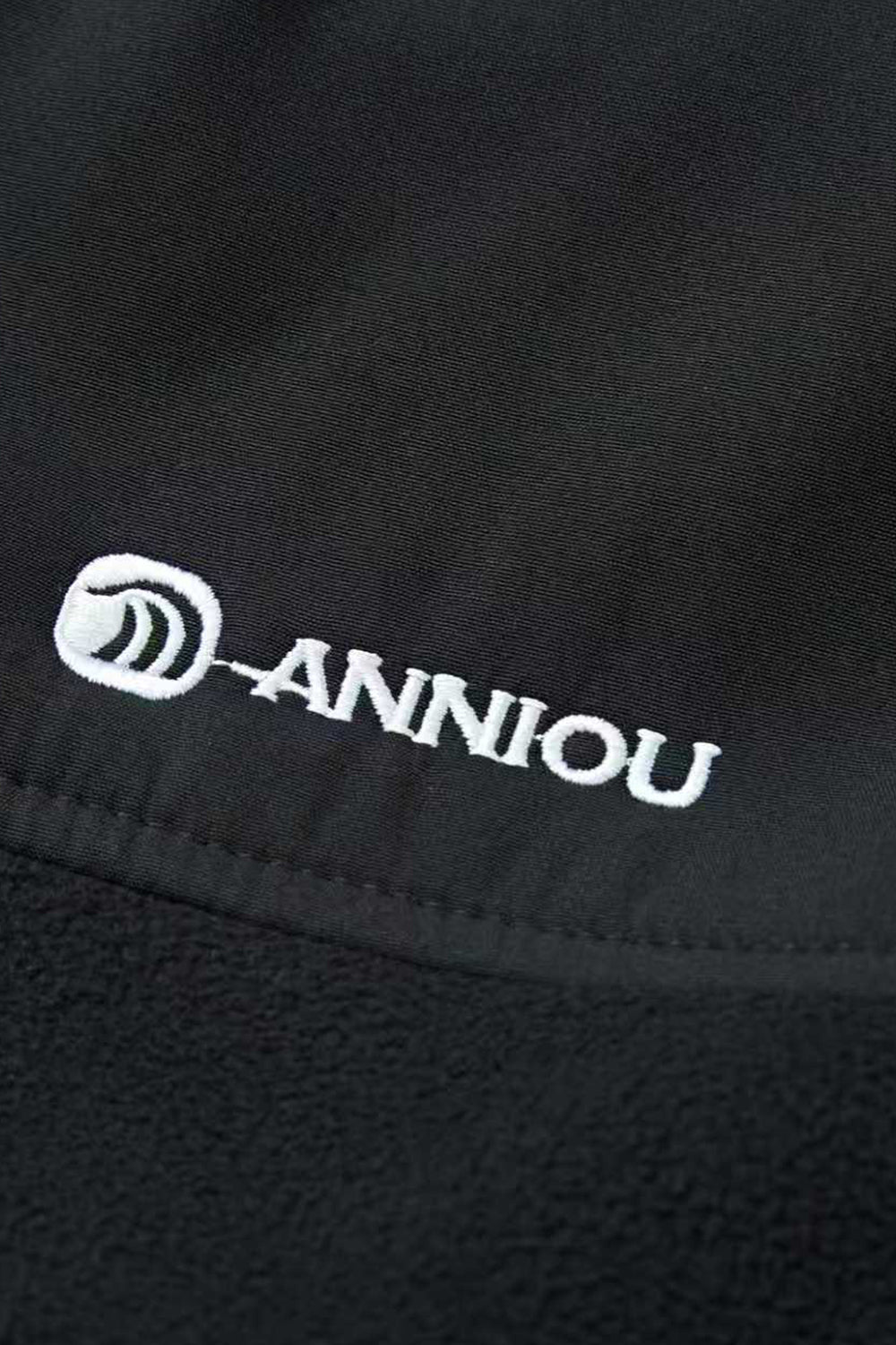 Close - up of a black fabric with 'Anniou' logo embroidered on it.