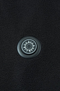 Round button with a sun design on a textured black background