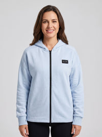 A woman wearing a light blue zip-up heated hoodie with a black front zipper.