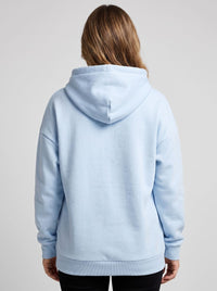 A woman viewed from the back wearing a light blue pullover hoodie against a plain light gray studio background.