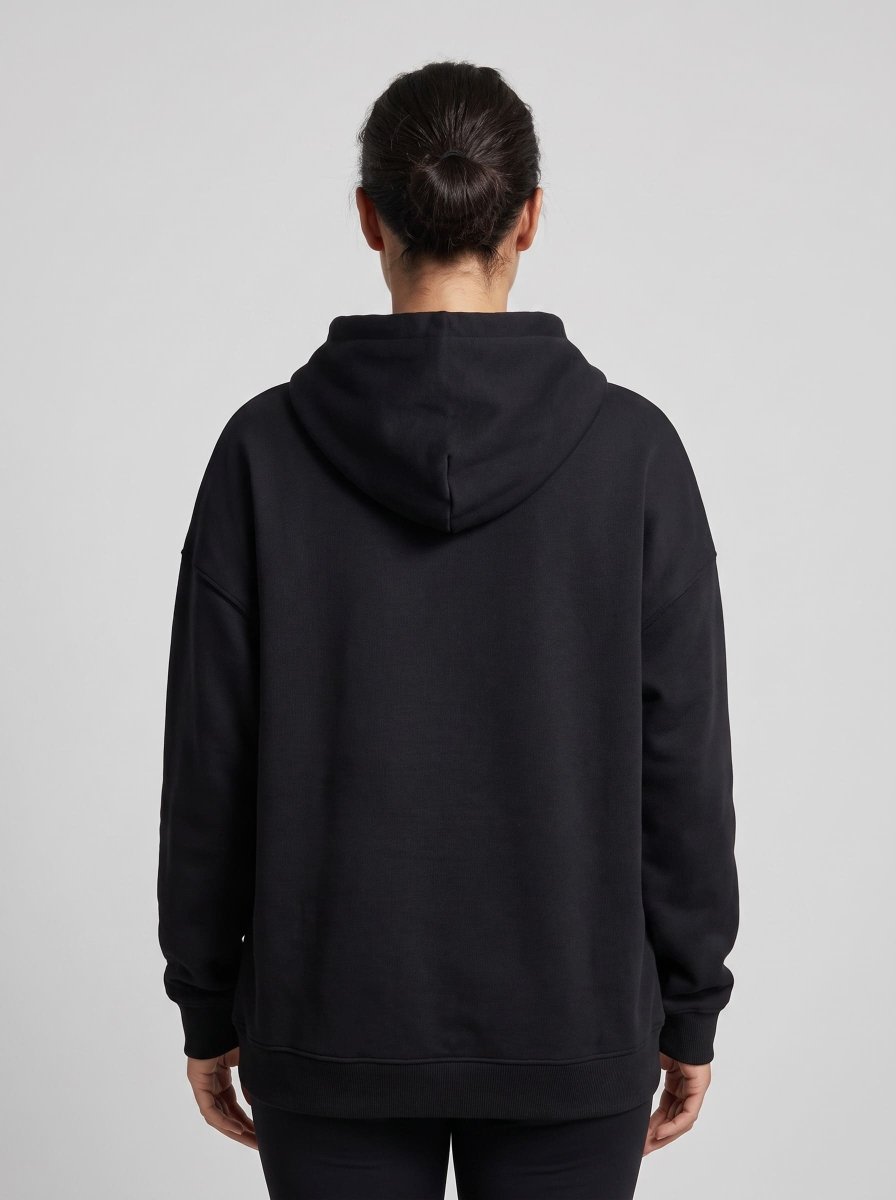 A person viewed from the back wearing an oversized black pullover hoodie against a light gray studio background.