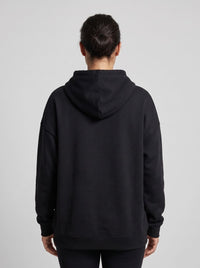 A person viewed from the back wearing an oversized black pullover hoodie against a light gray studio background.