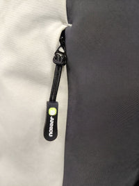 Close-up of a black zipper pull tab with a bright green circular logo and white vertical text reading 'ANNIOU' on a light gray fabric next to a dark gray panel.