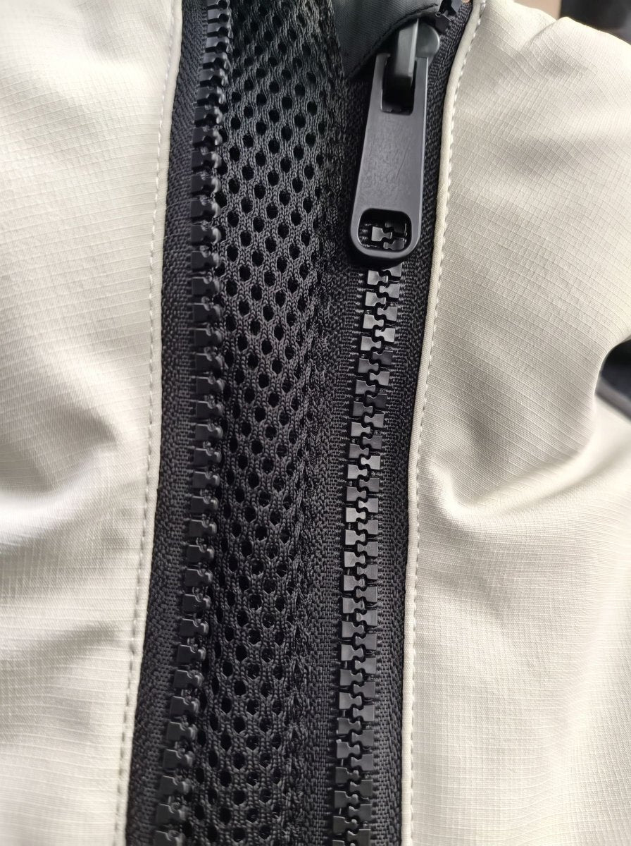 Close-up of a black mesh zipper panel on a light beige or off-white fabric ski jacket, showing the black zipper teeth and pull tab.