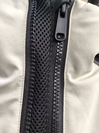 Close-up of a black mesh zipper panel on a light beige or off-white fabric ski jacket, showing the black zipper teeth and pull tab.