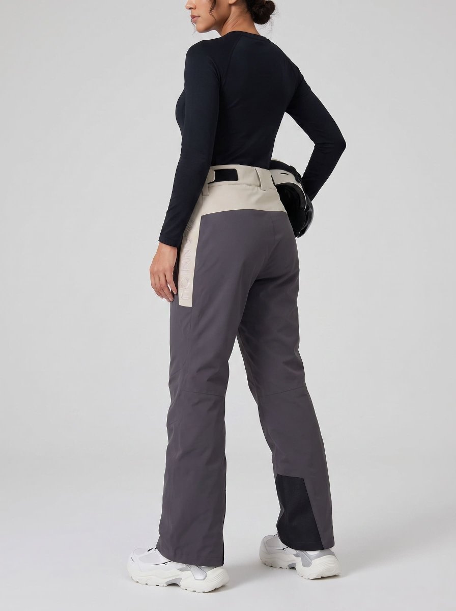 A woman shown from the back wearing colorblock ski pants in dark gray and beige, paired with a black long-sleeve top